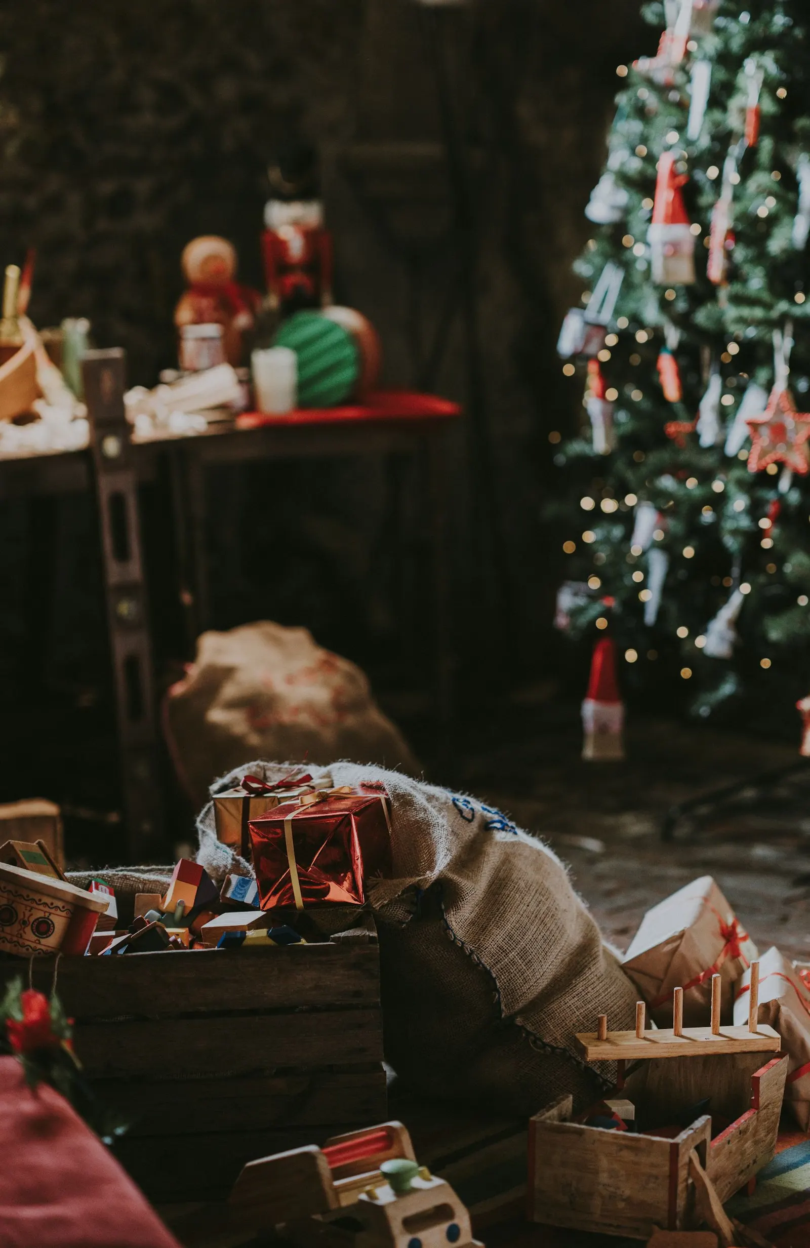 Jouets en bois, caisses et paquets cadeaux posés sur le sol au pied d'un sapin illuminé